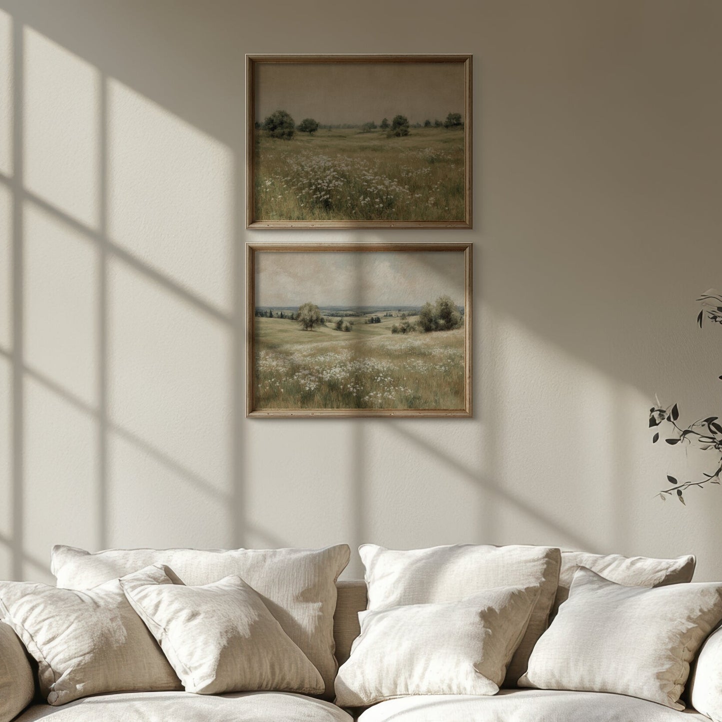 Beige sofa with white cushions in a room with sunlight streaming through a window, wall art, and a plant.