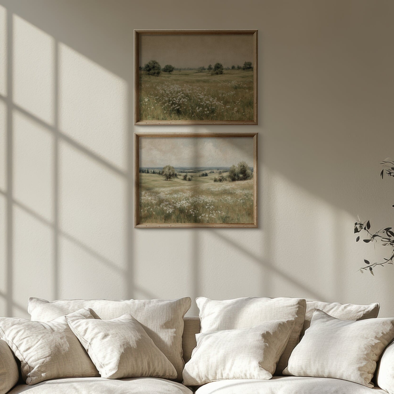 Beige sofa with white cushions in a room with sunlight streaming through a window, wall art, and a plant.