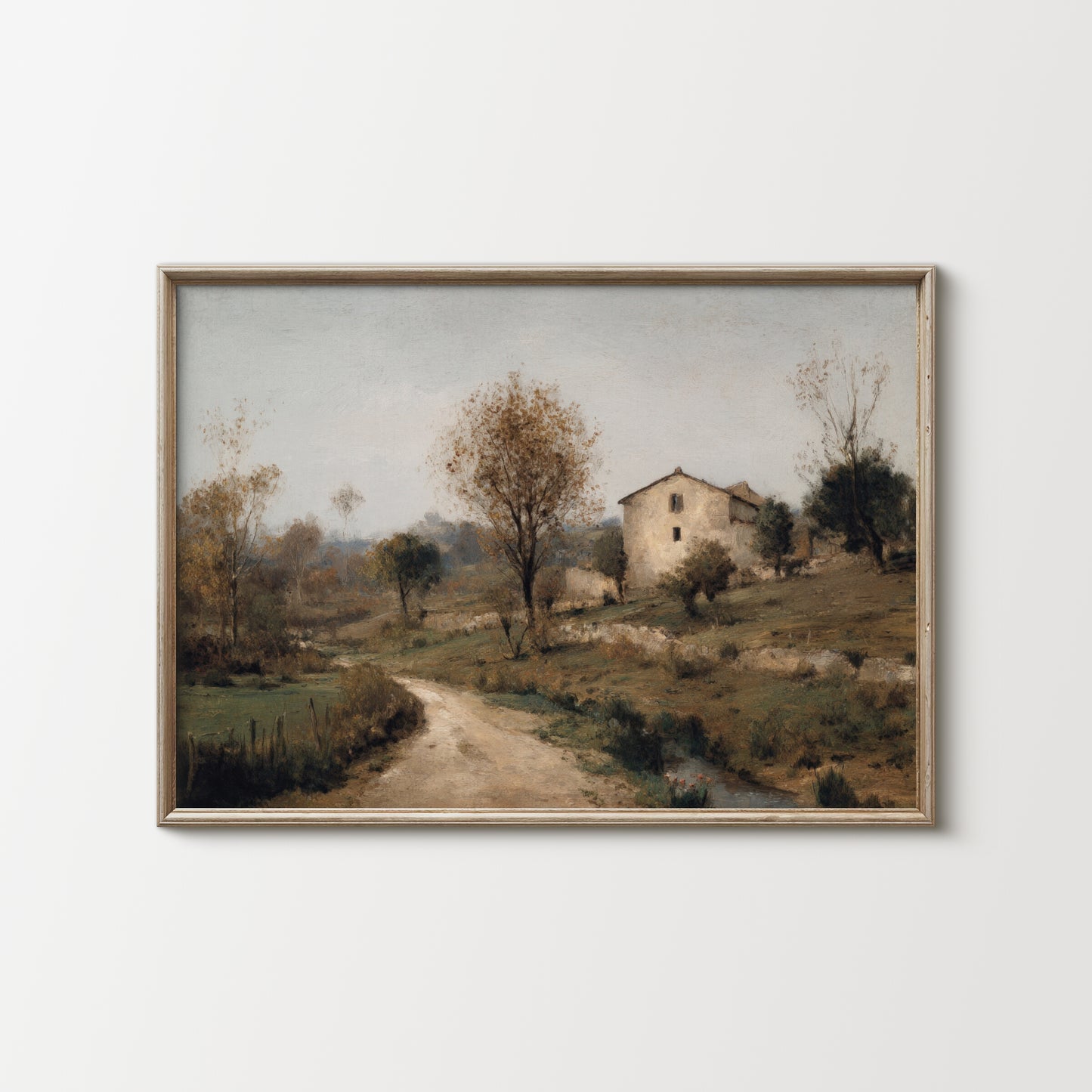 Framed landscape painting of a rural scene with a house and path on a white wall.