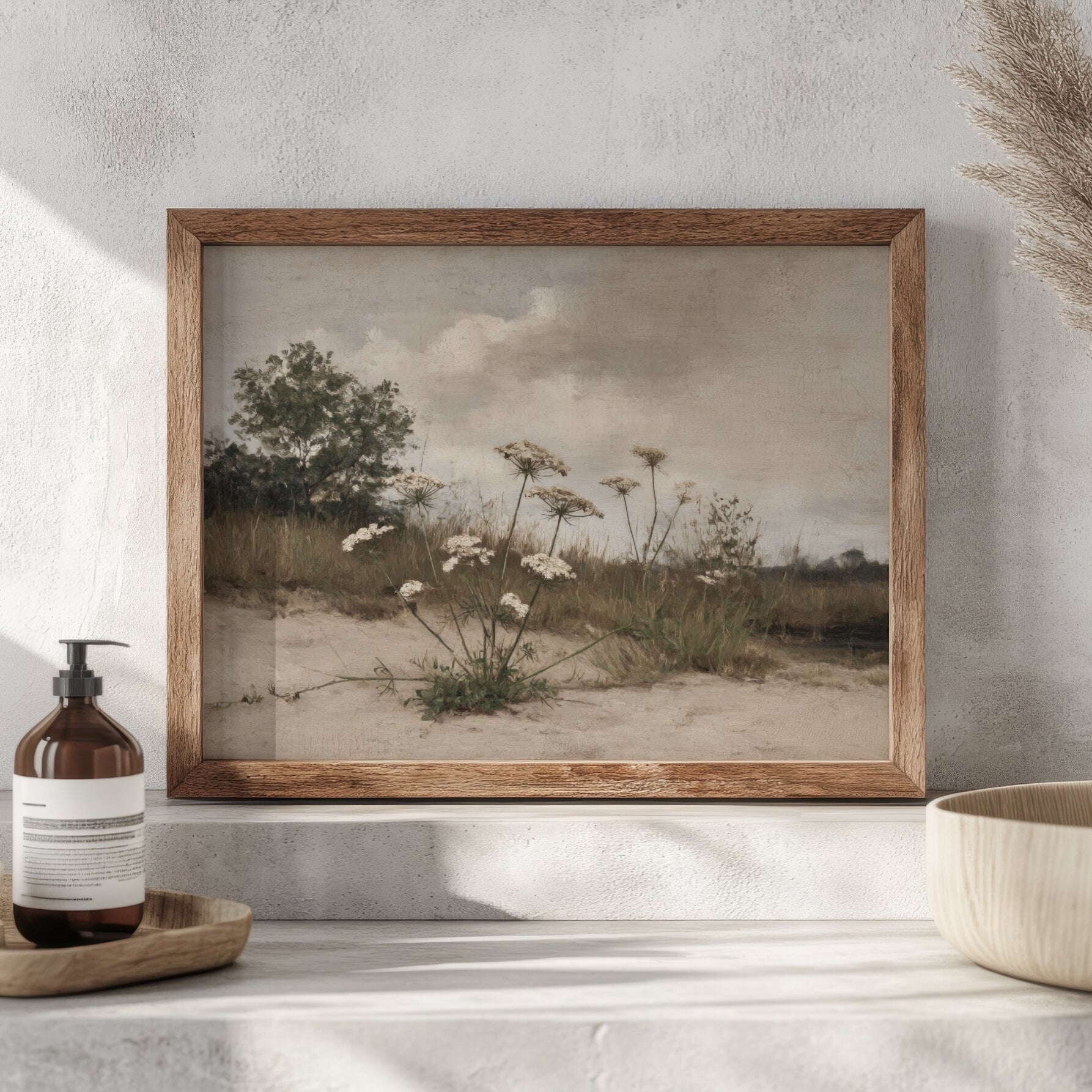 Framed landscape print of a field with flowers on a wall above a shelf.