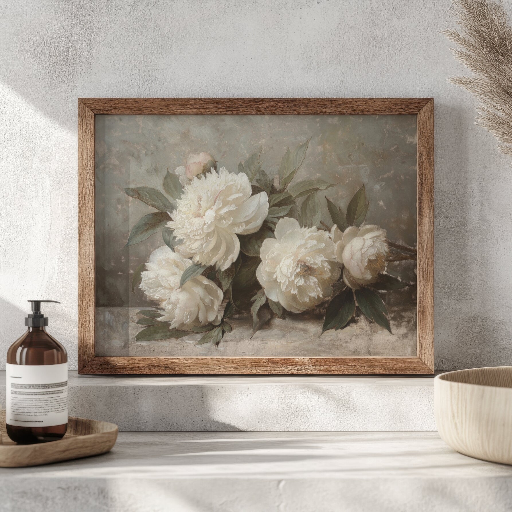 Framed floral artwork on a wall with a bottle and bowl below.