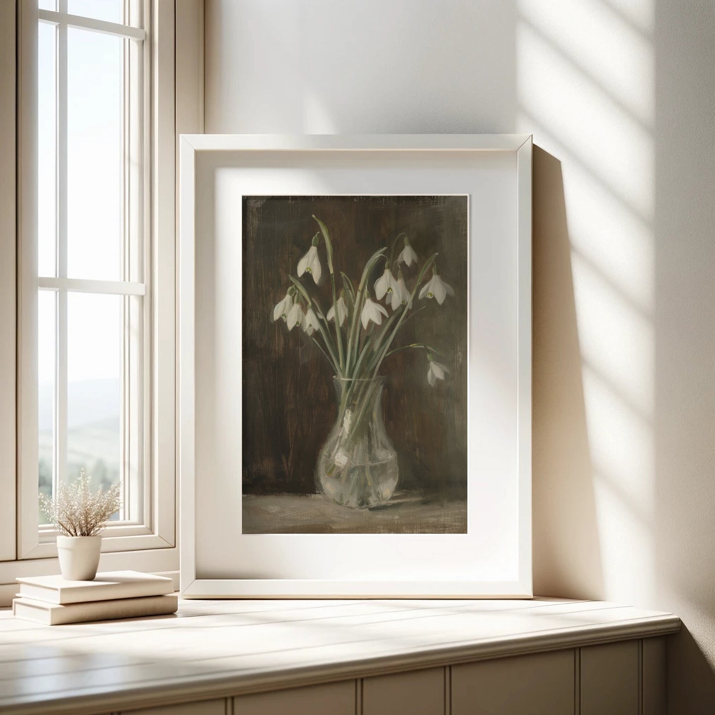 Framed artwork of snowdrops on a wooden surface with a window in the background