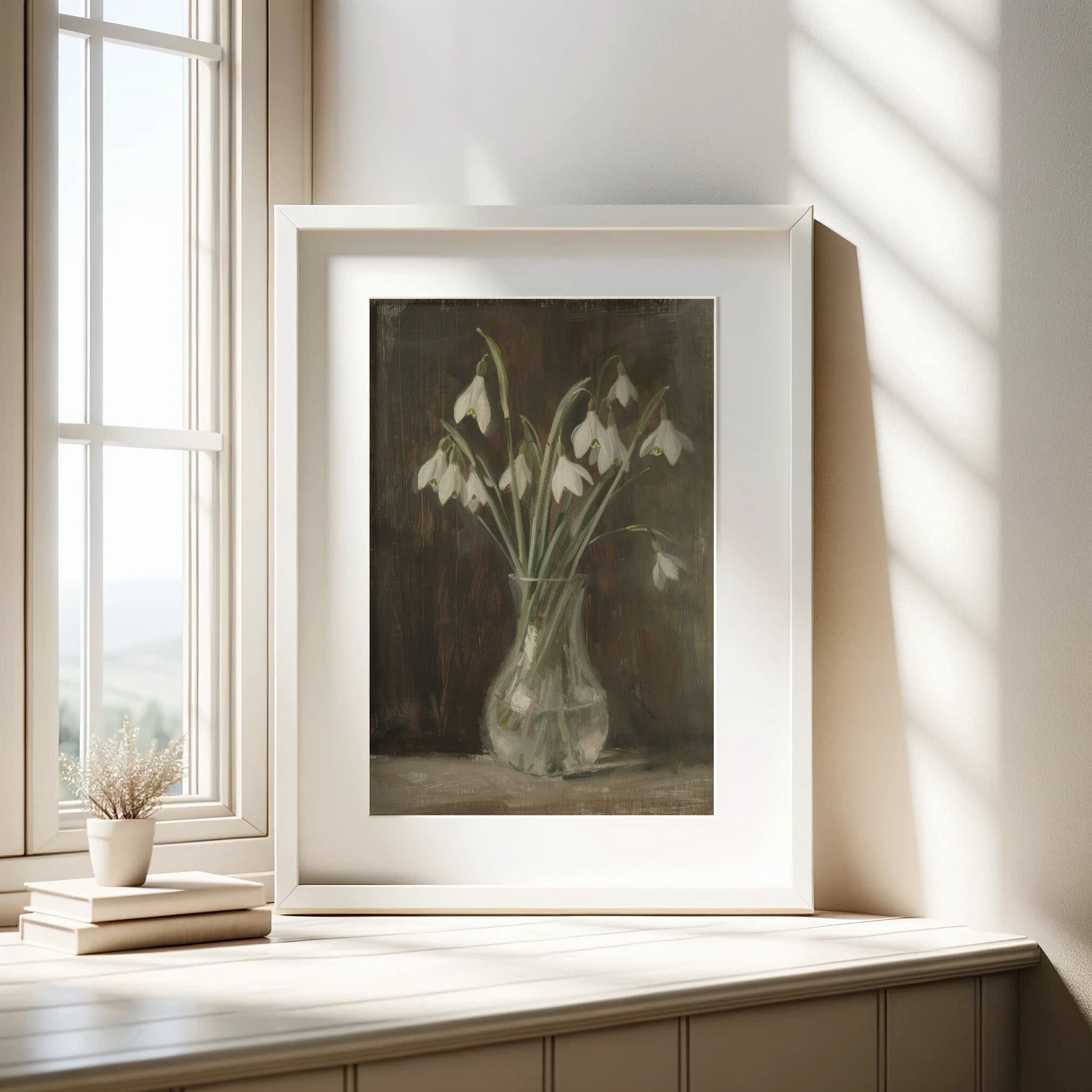 Framed artwork of snowdrops on a wooden surface with a window in the background