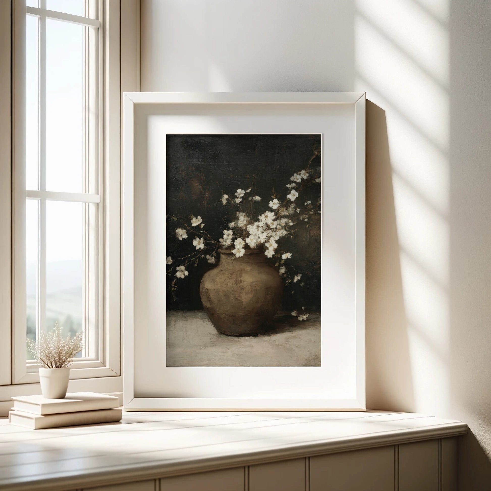 Framed artwork of a vase with flowers on a wooden surface near a window.