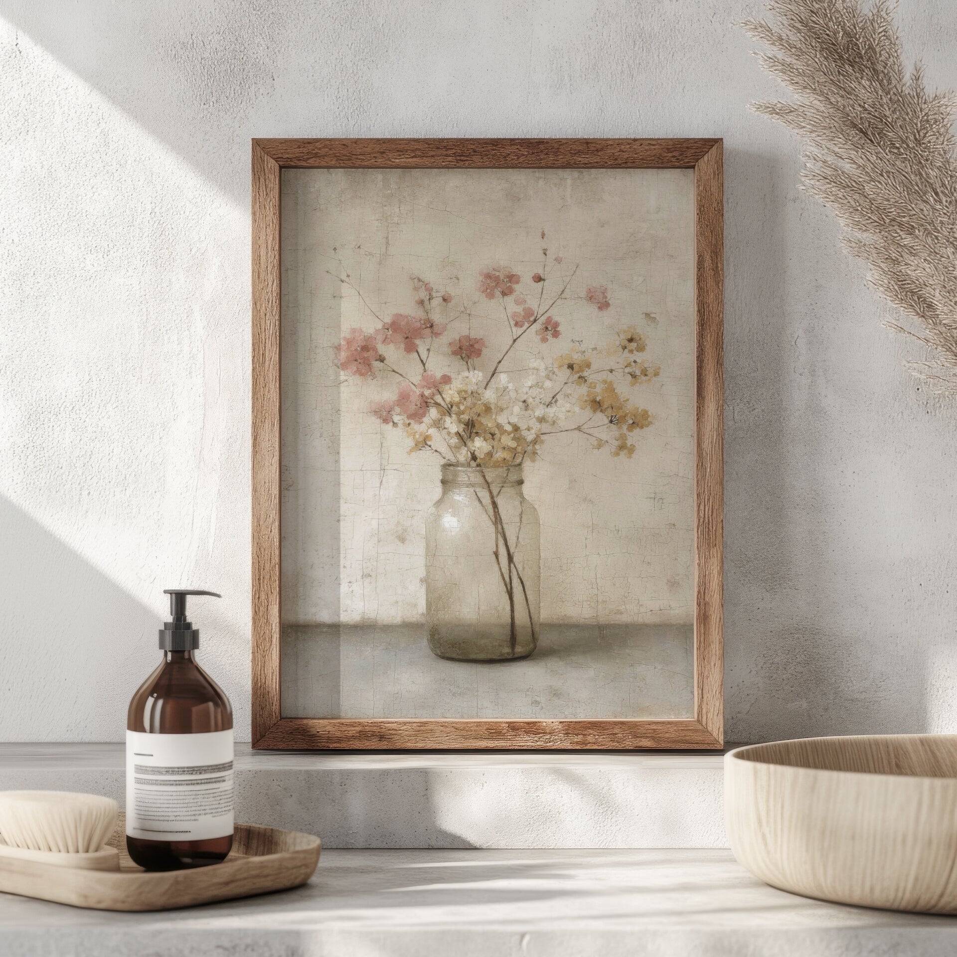 Framed artwork of a vase with flowers on a wall above a shelf with a bottle and bowl.