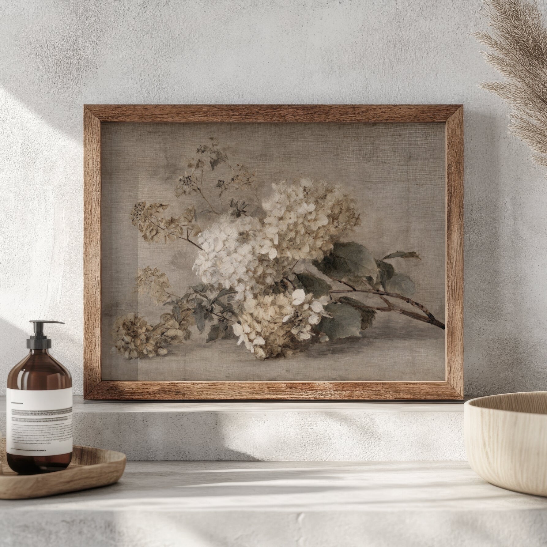 Framed floral artwork on a wall with a bottle and bowl in the foreground.
